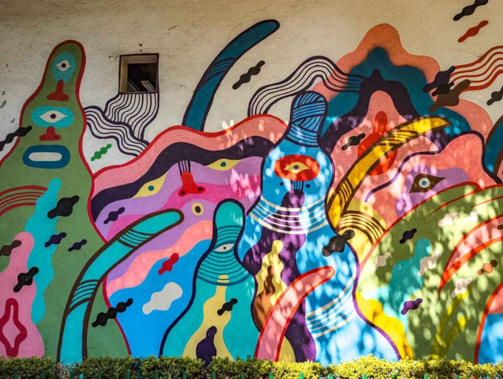 A colorful abstract street art painted on a wall in Mexico City depicts odd shaped figures with eyes.