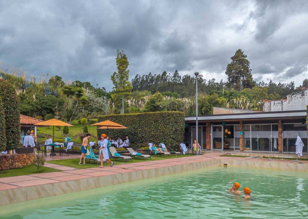 Outdoor hot spring pool at Novaqua in Cuenca Ecuador, with guests lounging under yellow umbrellas and enjoying the mineral-rich waters beneath cloudy skies.